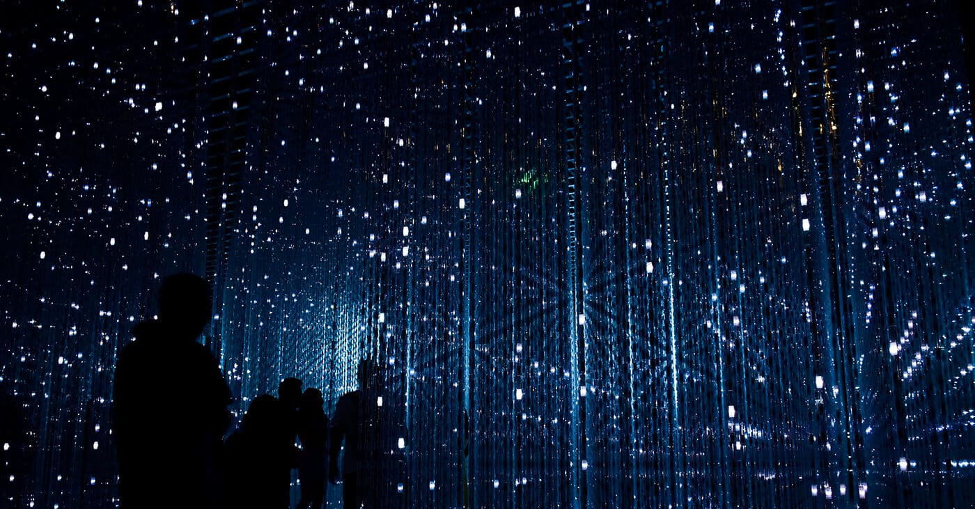 A group of people in an experiential exhibit with hundreds of small lights in a dark space